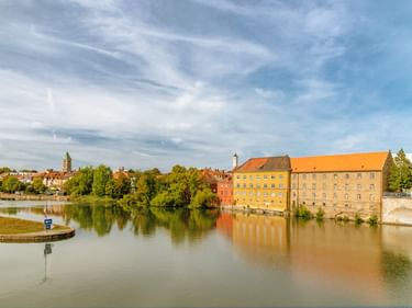Historische Gebäude am Main in Schweinfurt mit bunten Fassaden, die sich im ruhigen Wasser unter blauem Himmel mit Schleierwolken spiegeln.