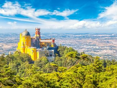 Palácio Nacional da Pena in Sintra mit gelben und roten Türmen über grünem Wald. Panoramablick auf das Tal unter blauem Himmel.