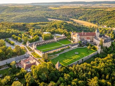 Luftaufnahme von Schloss Rosenburg mit befestigten Mauern, gepflegten Rasenflächen und kreisförmigem Gartenmuster, umgeben von dichten Wäldern.
