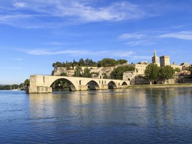 Die historische Brücke Pont d'Avignon mit vier Bögen über die Rhône, dahinter der Papstpalast und Befestigungsanlagen auf dem Hügel.