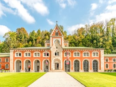 Alte Saline in Bad Reichenhall, ein symmetrisches Gebäude mit orange-weißer Fassade, Bogenfenstern und Kapellenturm, umgeben von grünem Rasen und Bäumen.