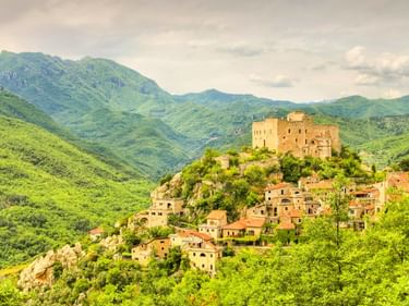 Castelvecchio di Rocca Barbena, ein mittelalterliches Bergdorf mit Steinburg und Häusern, umgeben von grünen Bergen in Italien.