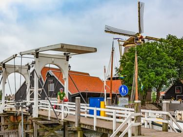 Weiße hölzerne Zugbrücke mit Hebevorrichtung in Harderwijk. Eine traditionelle Windmühle und Gebäude mit orangefarbenen Dächern im Hintergrund.