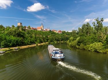Frachtschiff auf dem Neckar mit Blick auf die historische Stadt Bad Wimpfen auf einem Hügel mit Turm und Kirchturm zwischen roten Dächern.