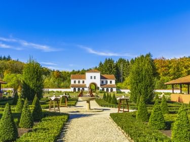 Weiße Villa im römischen Stil mit rotem Ziegeldach in Villa Borg in Perl. Gepflegte Gärten mit geschnittenen Hecken und Kiesweg führen zum Gebäude.