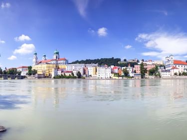 Panoramablick auf Passaus historische Altstadt mit bunten Gebäuden und Kirchtürmen entlang der Donau unter blauem Himmel.
