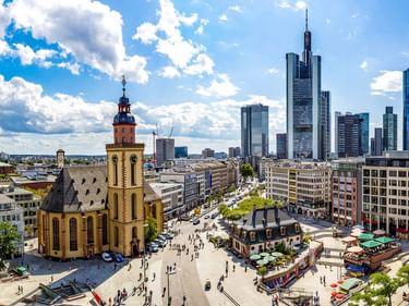 Frankfurt am Main Stadtansicht mit historischer Kirche im Vordergrund und modernen Wolkenkratzern im Hintergrund unter blauem Himmel mit weißen Wolken.
