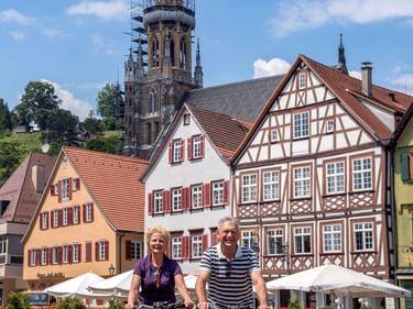 Zwei Radfahrer fahren über den Esslinger Marktplatz mit bunten Fachwerkhäusern und gotischem Kirchturm im Hintergrund.