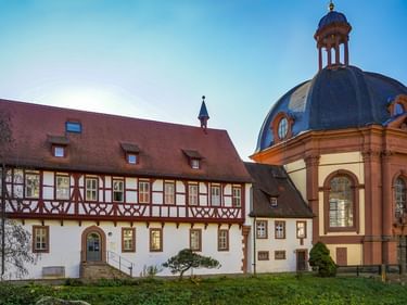 Klosteranlage Benediktushof in Holzkirchen mit Fachwerkgebäude und barocker Kapelle mit blauer Kuppel und Laternenturm.