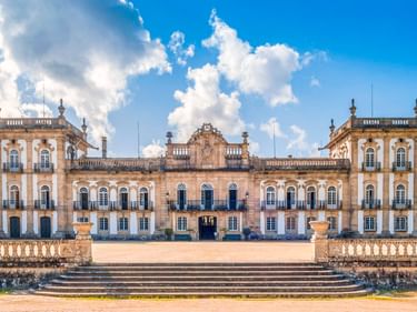 Palácio de Brejoeira, ein neoklassizistischer Palast in Monção mit symmetrischer Fassade, verzierten Balustraden und Steinstufen unter blauem Himmel.