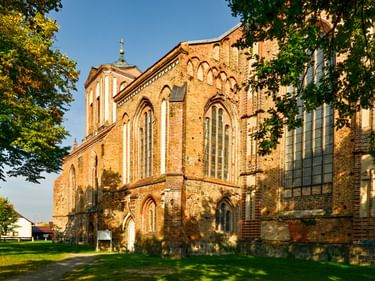 Gothic brick church in Gartz with pointed arch windows and tower, framed by green trees under blue sky. The red brick facade shows weathered surfaces.