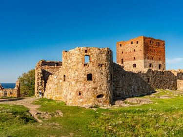 Mittelalterliche Burgruine Hammershus auf Bornholm mit Steinmauern und Türmen vor blauem Himmel, mit Blick auf die Ostsee und grünem Gras.