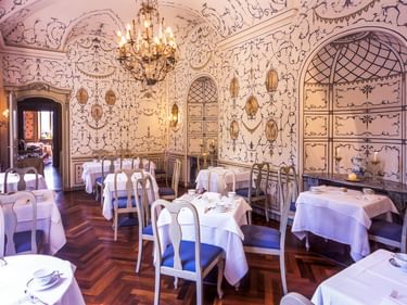 Eleganter Speisesaal in der Villa Matilde mit kunstvollen Wanddekorationen, Kronleuchter, weißen Tischdecken und dekorativen Bogenschränken.