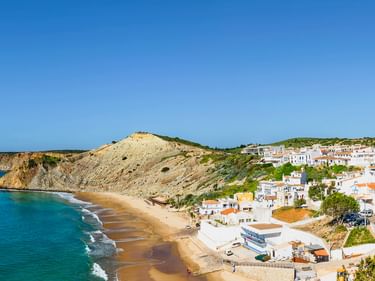 Panoramablick auf Burgau, ein weißes Dorf auf Klippen über einem Sandstrand. Türkisfarbenes Meer und felsige Landzungen unter blauem Himmel.