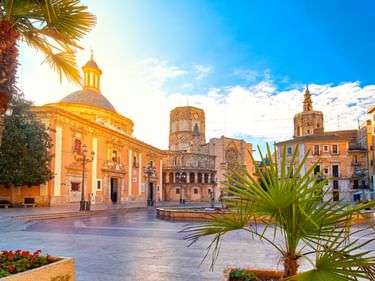 Plaza de la Virgen in Valencia mit historischer Kathedrale, Glockenturm und Palmen unter blauem Himmel. Der Platz zeigt prachtvolle Architektur.