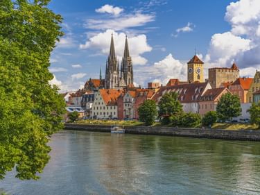 Regensburger Altstadt mit dem Dom und mittelalterlichen Türmen an der Donau unter blauem Himmel mit weißen Wolken.