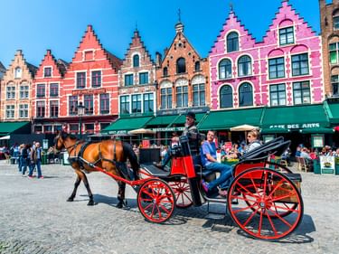 Schwarze Pferdekutsche mit roten Rädern auf dem Grote Markt in Brügge, mit bunten historischen Giebelhäusern und Straßencafés im Hintergrund.