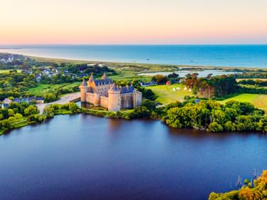 Luftaufnahme von Schloss Suscinio auf der Halbinsel Rhuys, umgeben von Wasser und grünen Feldern. Die mittelalterliche Festung steht bei Sonnenuntergang nahe der Küste.
