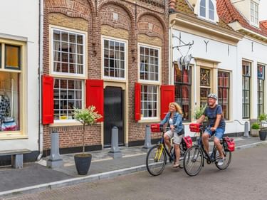 Zwei Radfahrer fahren durch eine historische Straße in Harderwijk mit traditionellen niederländischen Gebäuden mit roten Backsteinfassaden und roten Fensterläden.