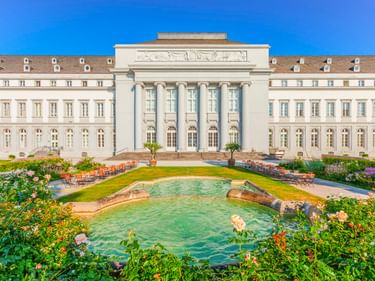 Kurfürstliches Schloss in Koblenz mit neoklassizistischer Fassade, Säuleneingang und formellem Garten mit Brunnen und bunten Blumen.