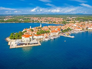 Luftaufnahme von Porec, Kroatien, mit historischer Halbinsel mit orangefarbenen Dächern, Kirchturm, Hafen und blauer Adria.