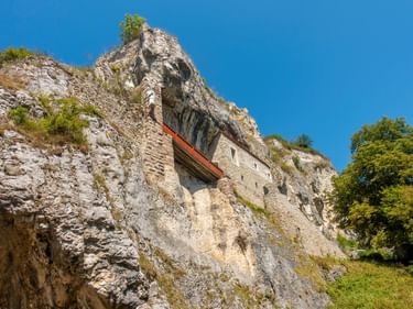 Historische Steinkapelle in die weiße Kalksteinklippe des Isteiner Klotz in Efringen-Kirchen gebaut, umgeben von grüner Vegetation unter blauem Himmel.