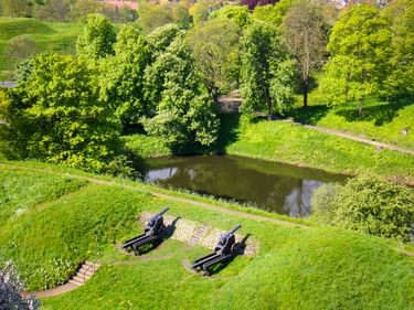 Luftaufnahme von zwei historischen Kanonen auf Graswällen der Festung Fredericia mit Wassergraben, Spazierwegen und grünen Bäumen in Dänemark.