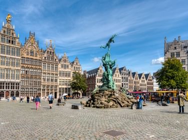 Brabobrunnen mit Bronzestatue auf dem Grote Markt in Antwerpen, umgeben von historischen Giebelhäusern unter blauem Himmel mit Besuchern.
