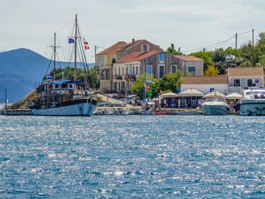 Hafenansicht von Fiskardo auf Kefalonia mit Booten am Ufer, traditionellen Gebäuden mit Terrakottadächern und Bergen im Hintergrund.