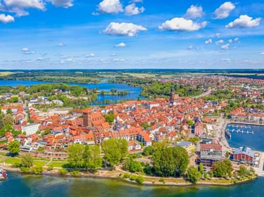 Luftaufnahme von Waren an der Müritz mit roter Altstadt, Kirchturm, Hafen und blauen Seen unter sonnigem Himmel.