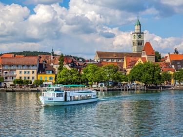 Passagierboot auf dem Bodensee vor Überlingen. Historische Gebäude mit roten Dächern und Kirchturm mit grüner Spitze unter blauem Himmel.