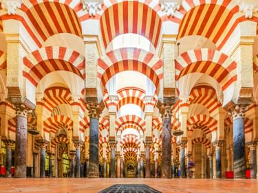 Innenraum der Mezquita-Kathedrale in Córdoba mit Säulenreihen und charakteristischen rot-weiß gestreiften Hufeisenbogen in symmetrischer Perspektive.