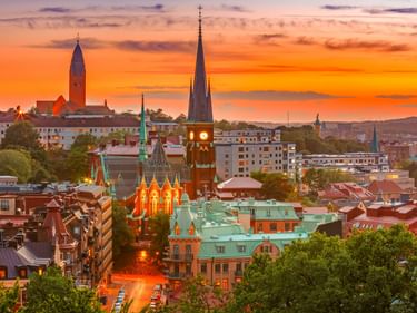 Panoramablick auf Göteborg bei Sonnenuntergang mit Kirchtürmen und bunten Gebäuden unter einem orange-violetten Himmel.