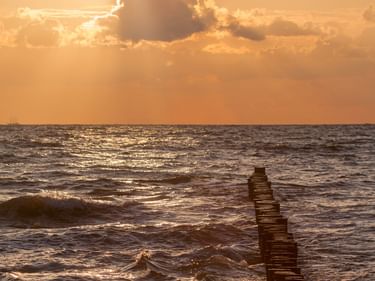 Hölzerne Buhne ragt in den Atlantik bei Sonnenuntergang mit goldenen Wolken und Sonnenstrahlen, Wellen umspülen die Struktur.