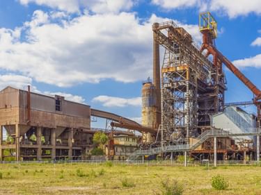 Industriekomplex im Parc du Haut-Fourneau in Uckange mit verrosteten Hochofenstrukturen, Metalltürmen und Fördersystemen unter blauem Himmel.