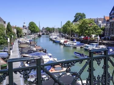 Kanal im Hafen von Dordrecht mit festgemachten Booten entlang hölzerner Stege. Historische niederländische Häuser säumen beide Seiten.