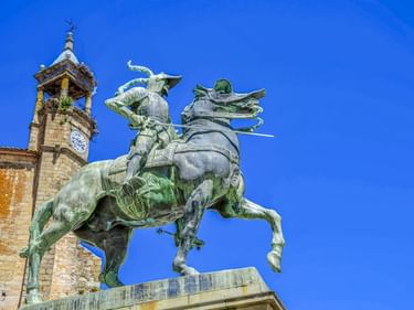 Bronzene Reiterstatue von Francisco Pizarro auf steigendem Pferd vor klarem blauen Himmel. Historischer Glockenturm im Hintergrund in Trujillo.