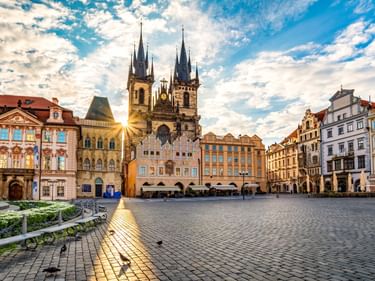 Altstädter Ring in Prag mit den gotischen Zwillingstürmen der Teynkirche über bunten historischen Gebäuden unter blauem Himmel mit Wolken.