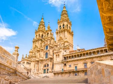 Steintreppe zur Kathedrale von Santiago de Compostela mit verzierten barocken Türmen unter blauem Himmel.