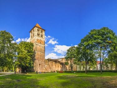 Stone tower and ruins of Bad Hersfeld Abbey surrounded by green lawn and trees under blue sky. Historic Romanesque church remains in Germany.