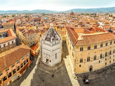 Luftaufnahme von Pistoias historischem Zentrum mit gestreiftem Baptisterium, Terrakottadächern und Bergen am Horizont.