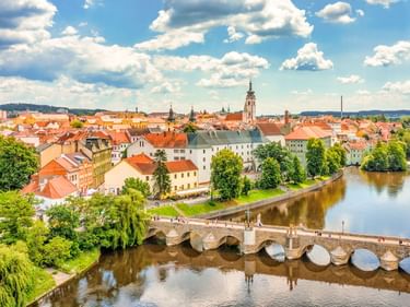 Luftaufnahme von Písek, Tschechien, mit historischer Steinbrücke über einem Fluss, bunten Gebäuden und Kirchturm unter blauem Himmel.