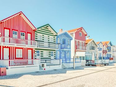 Reihe traditioneller gestreifter Häuser in Costa Nova mit roten, grünen und blauen vertikalen Streifen auf weißen Fassaden unter blauem Himmel.