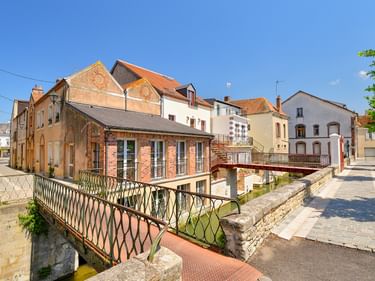 Dekorative Metallbrücke über einen Kanal in der Altstadt von Montargis, mit bunten historischen Gebäuden und klarem blauen Himmel.