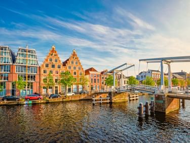Weiße Zugbrücke Gravestenenbrug über Kanal in Haarlem mit historischen niederländischen Giebelhäusern und modernen Gebäuden am Ufer unter blauem Himmel.