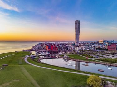 Luftaufnahme der Malmöer Uferpromenade bei Sonnenuntergang mit dem gedrehten Turning Torso Wolkenkratzer über Wohngebäuden und einem Jachthafen.