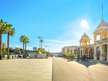 Sonnige Promenade in Viareggio mit hohen Palmen links und eleganten historischen Gebäuden mit Türmen rechts unter blauem Himmel.