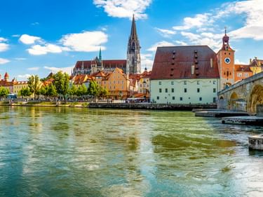 Panoramablick auf die historische Steinerne Brücke in Regensburg über die Donau mit mittelalterlichen Türmen, Kirchtürmen und bunten Gebäuden.