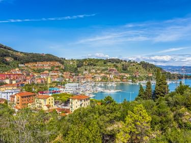 Panoramablick auf La Spezia mit bunten Häusern an Hängen, einem Yachthafen mit Segelbooten und dem blauen Golf von La Spezia unter klarem Himmel.