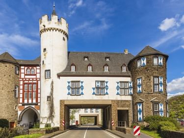Vorburg von Schloss von der Leyen in Kobern-Gondorf mit weißem Turm, Fachwerkfassade und Straße durch das Torgebäude.